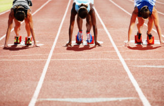 Three female runners poised at the starting blocks